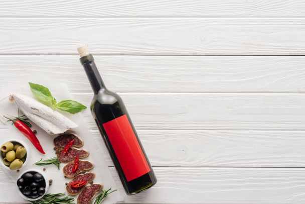top view of bottle of red wine and assorted meat snacks on white wooden tabletop - Photo, Image