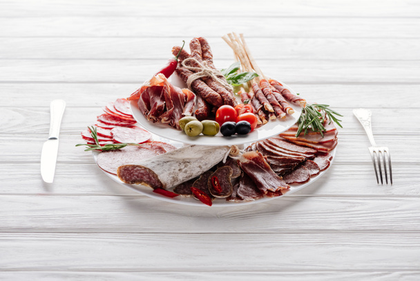 close up view of delicious meat appetizers with olives and rosemary on white wooden tabletop - Foto, imagen