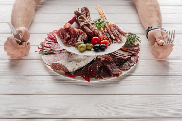 partial view of man with cutlery at white wooden tabletop with various meat snacks - Photo, Image