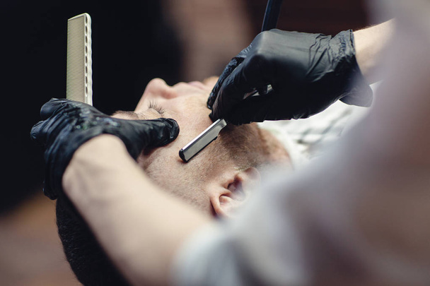 Hairdresser in black gloves shaves the razor's beard of the client - Photo, image