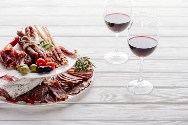 zbliżenie okulary czerwone wino i przekąski pyszne mięso na biały blat drewniany - Zdjęcie, obraz