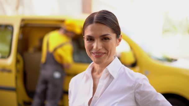 Smiling businesswoman is showing thumb up. Blurred delivery van and courier at the background - Кадри, відео