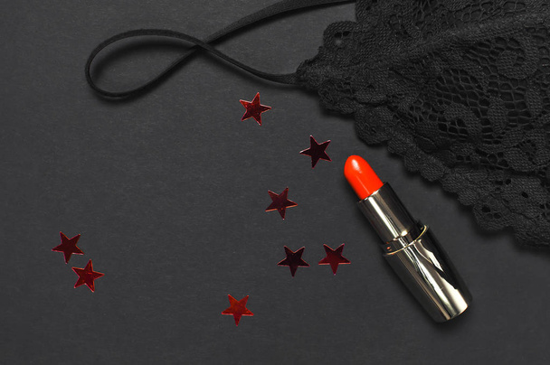 Black lace bra underwear, red lipstick, holographic confetti on dark background top view flat lay. Female essential erotic accessories, fashionable underwear gift for birthday new year christmas - Photo, Image