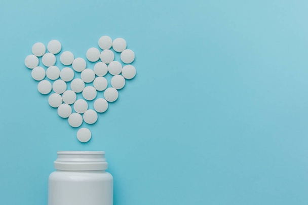 Gyógyszerek fehér, kerek szív alakú tabletták elszigetelt kék háttér. - Fotó, kép