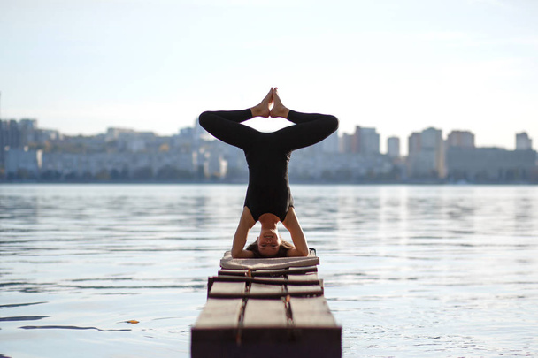 Jeune femme pratiquant l'exercice de yoga à quai en bois calme avec fond de ville. Sport et loisirs en ville
. - Photo, image