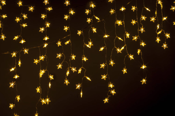 Un rideau de guirlande en forme d'étoiles est accroché sur un fond sombre
. - Photo, image