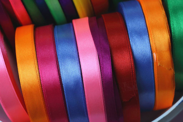 Много красивых цветных атласных лент вид сверху для украшения, упаковки подарков и шитья в магазине ткани яркий и красочный фон закрыть
 - Фото, изображение
