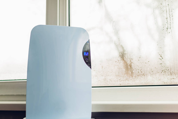 Luftentfeuchter mit Touchpanel, Feuchtigkeitsanzeige, UV-Lampe, Luftionisator, Wasserbehälter funktioniert durch nasses Fenster in der Wohnung. Nahaufnahme - Foto, Bild
