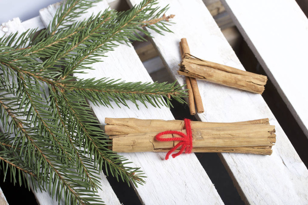 Cinnamon sticks next to the fir branches. On a wooden box. - Foto, afbeelding