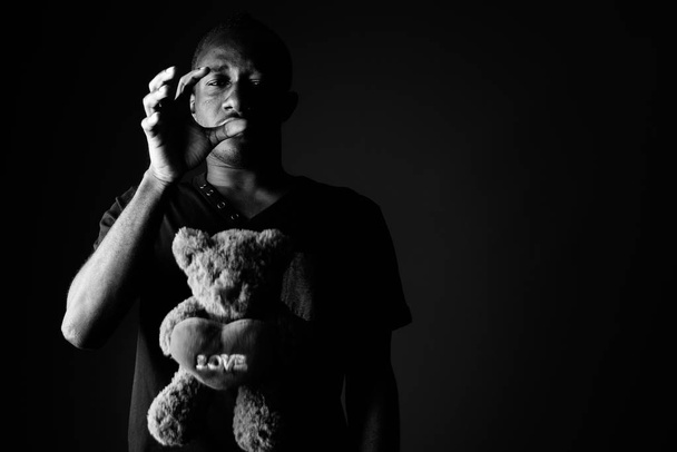 Грустный депрессивный молодой африканский мужчина с плюшевым мишкой и надписью любви в черно-белом
 - Фото, изображение