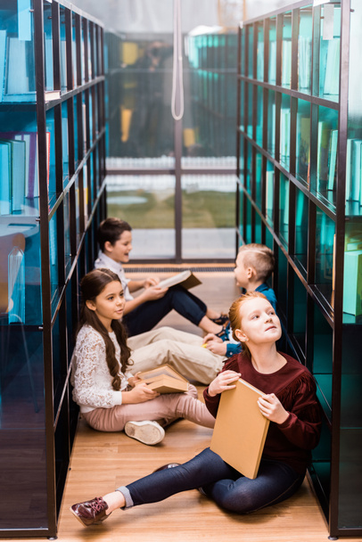 vista ad alto angolo di adorabili scolari che leggono libri sul pavimento in biblioteca
  - Foto, immagini