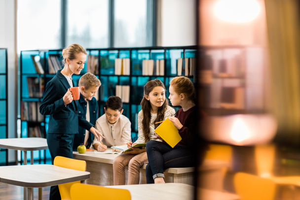 foco seletivo de crianças em idade escolar e bibliotecário conversando juntos na biblioteca
  - Foto, Imagem