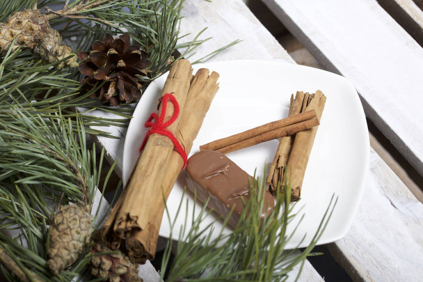 Cinnamon sticks and chocolate next to the pine twigs and cones. On a wooden box. - Foto, Imagem