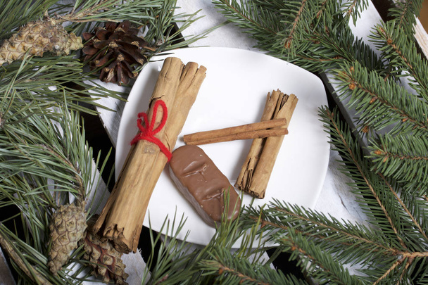 Kaneelstokjes en chocolade naast de pijnboom takjes en kegels. Op een houten doos. - Foto, afbeelding