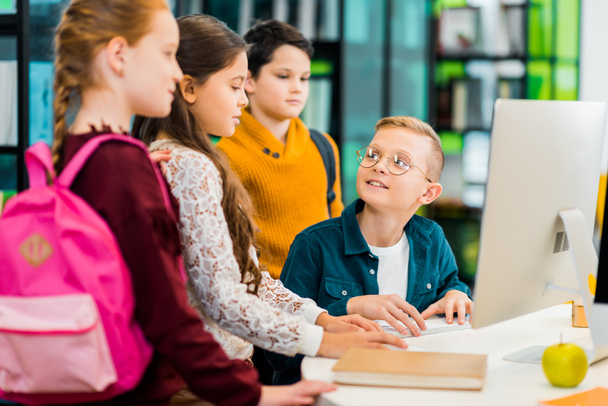 мальчик с помощью настольного компьютера и глядя на одноклассников в библиотеке
 - Фото, изображение