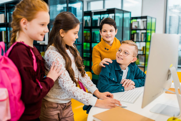 mignon sourire écoliers en utilisant ordinateur de bureau ensemble dans la bibliothèque
 - Photo, image