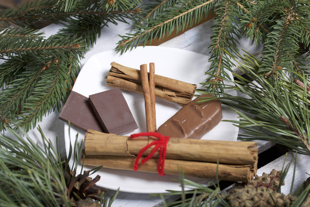 Cinnamon sticks and chocolate next to the pine twigs and cones. On a wooden box. - Fotografie, Obrázek