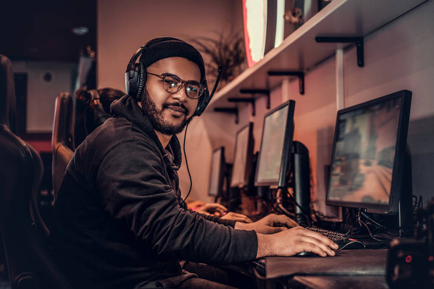 Un joven afroamericano, disfrutando pasar tiempo con sus amigos, jugando en un videojuego multijugador en un PC en un club de juegos o cibercafé
. - Foto, imagen