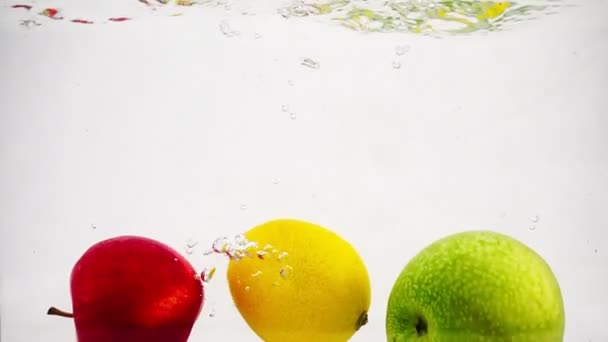 La manzana, el limón y el naranja caen en el agua con burbujas en movimiento lento. Frutos aislados de un fondo blanco. - Imágenes, Vídeo