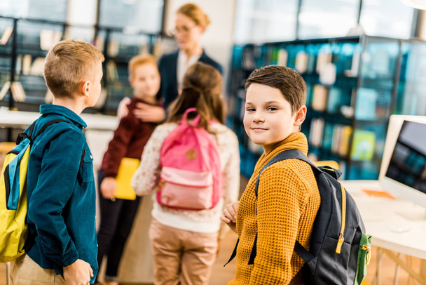 boy with backpack looking at camera while visiting library with classmates  - Valokuva, kuva