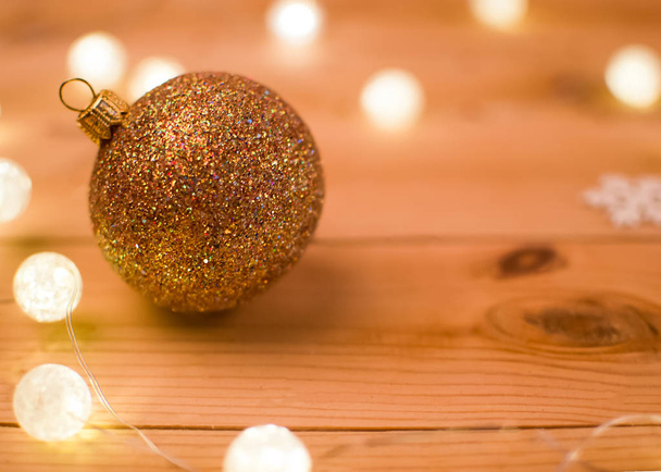 Bola de Natal dourada em um fundo de madeira cercado por luzes de guirlanda
. - Foto, Imagem