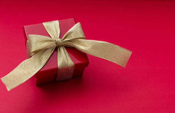 Christmas or valentines day gift box. Red gift with shiny gold ribbon on red background, view from above, copy space - Fotografie, Obrázek