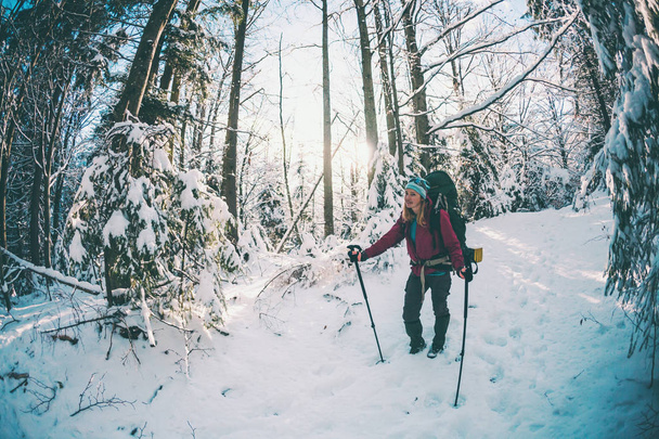Kış dağlarında sırt çantalı ve kar ayakkabılı bir kadın. Manzaralı yerlere git. Yürüyüş sopalı bir sarışın. Karlı bir ormanda bir turist yürüyor. Kız yol boyunca yürür. - Fotoğraf, Görsel