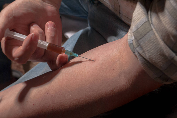 Injektion eines Medikaments in den Arm einer Person mit einer Spritze in die Blutvene - Foto, Bild