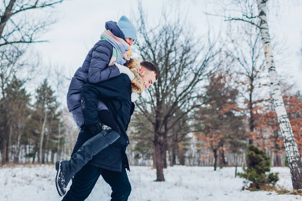 Un tipo dando a su novia a cuestas en el bosque de invierno. Joven pareja amorosa divirtiéndose al aire libre. Gente feliz relajándose
 - Foto, Imagen