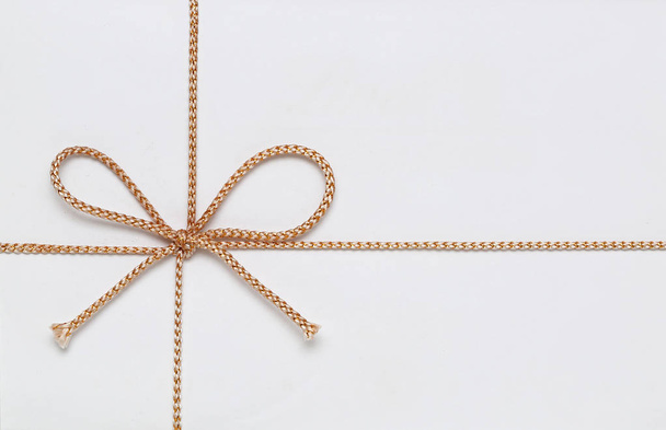 Pequeño arco de cuerda dorada en caja de regalo blanca
 - Foto, imagen