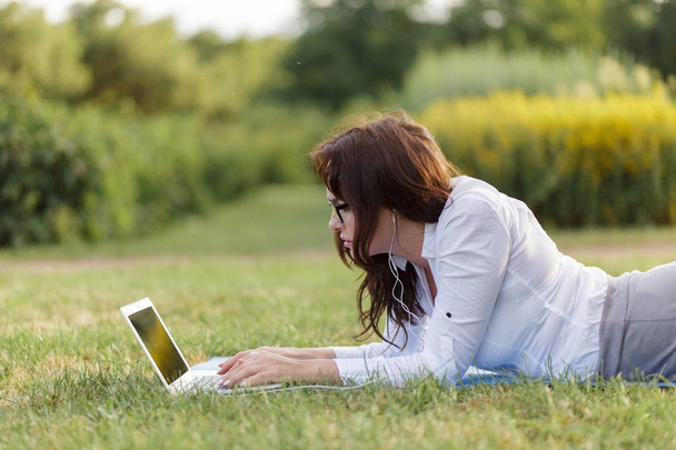 Business girl laying on green grass and working using her laptop in the park - Fotó, kép