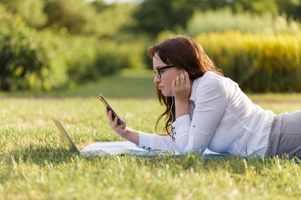 Business girl laying on green grass and working using her laptop in the park - 写真・画像