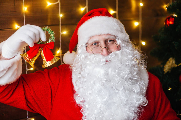 Santa Claus ringing a bell near Christmas tree with gifts - Фото, изображение