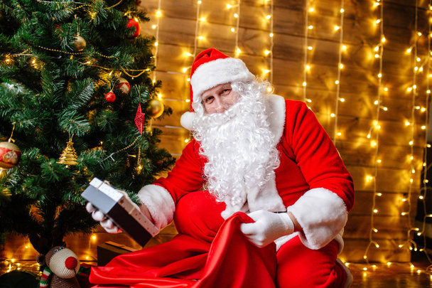 Santa Claus near Christmas tree with gifts. Christmas time - Фото, изображение