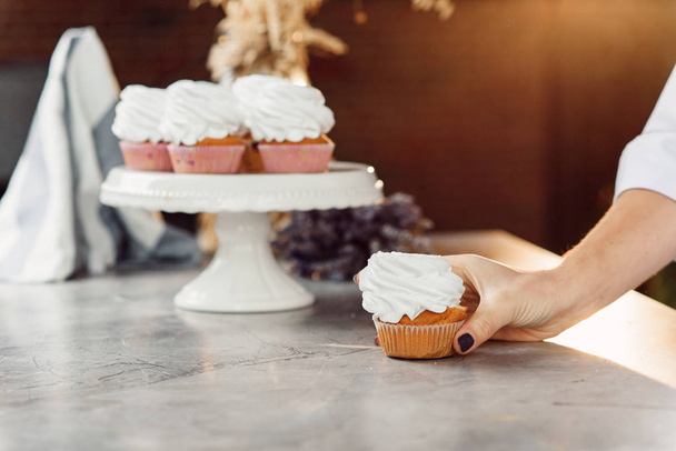 Close up woman's hand holds a fresh tasty cupcake with a white cream and puts it on a white tray. - Foto, Imagen