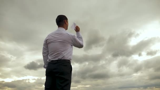Biznesmen w białej koszuli bawi się z papieru latanie samolotem na tle ciemnych chmur. Zwolnionym tempie - Materiał filmowy, wideo