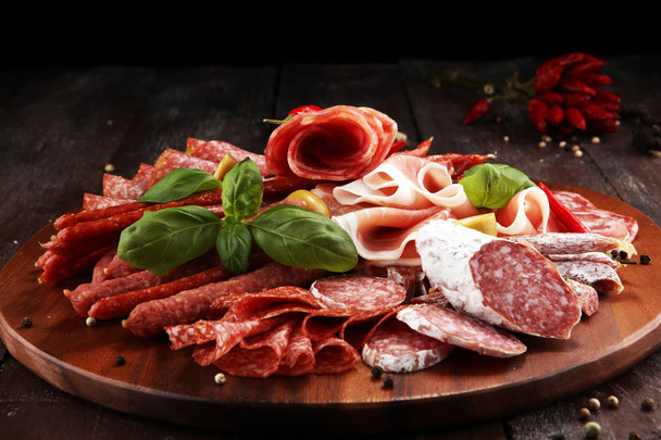 Food tray with delicious salami, pieces of sliced prosciutto crudo, sausage and basil. Meat platter with selection. - Photo, Image