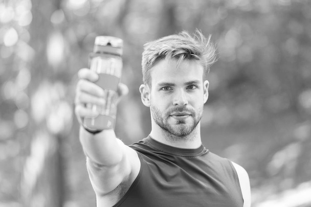 Man with athletic appearance holds bottle with water. Man athlete in sport clothes training outdoor. Sport and healthy lifestyle concept. Athlete drink water after training at stadium on sunny day - Foto, afbeelding