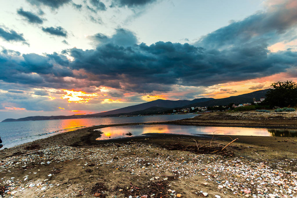 Mar à beira-mar ao pôr-do-sol com sol escondido e nuvens coloridas
 - Foto, Imagem