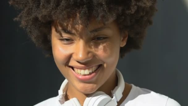 Curly-haired lady in earphones sincerely flirting and smiling, touching hair - Filmagem, Vídeo