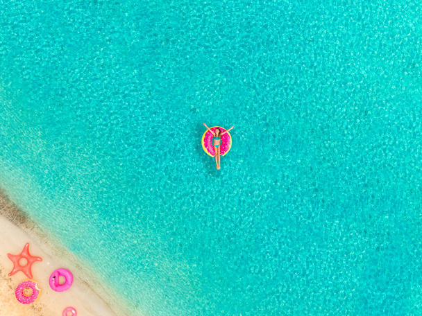 Luftaufnahme eines Mädchens, das auf aufblasbarer Donut-Matratze am Sandstrand und aufblasbaren Ringen schwimmt. - Foto, Bild