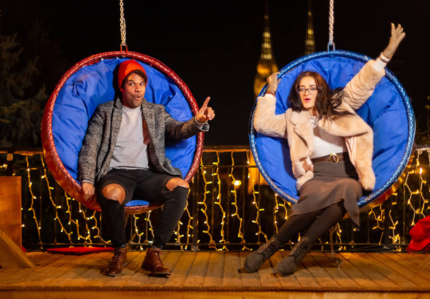 Couple having fun on hanging Christmas chairs, Zagreb, Croatia. - Foto, immagini