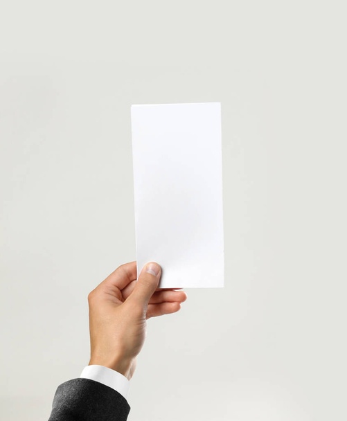 Male hands in white shirt and black jacket holding a white sheet of paper. Isolated on gray background. Closeup. - Fotografie, Obrázek
