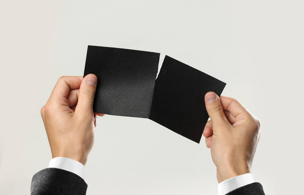 Male hands in white shirt and black jacket rip a black sheet of paper. Isolated on gray background. Closeup. - Foto, Bild