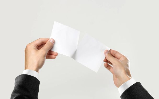 Male hands in white shirt and black jacket rip a white sheet of paper. Isolated on gray background. Closeup. - Foto, Imagem