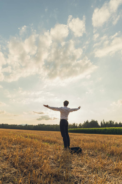 Young businessman standing in the middle of a sawn field under beautiful sky with his arms spread widely. - Fotó, kép