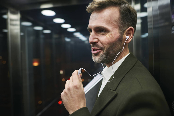 Side view of happy businessman listening to music in elevator  - Zdjęcie, obraz