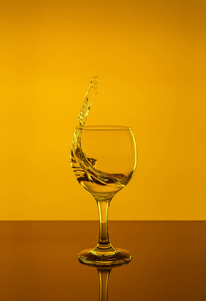 Splash of wine in a glass. Drink in glass on a yellow background. - Фото, зображення