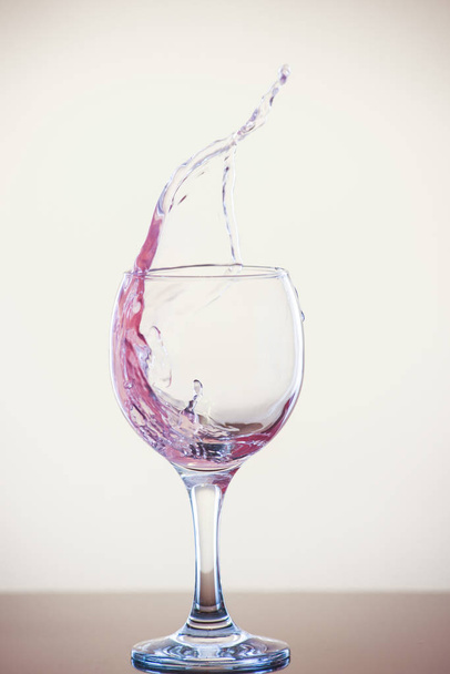 Splash of wine in a glass. Pink drink in glass on a white background. - Фото, изображение
