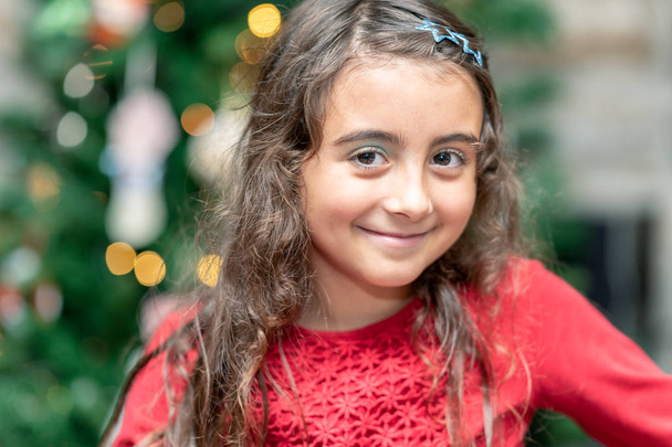 Gelukkig jong meisje tegenover kerstboom thuis. - Foto, afbeelding